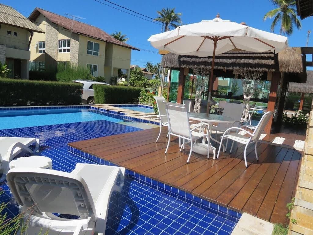 Deck da piscina com mesa, guarda-sol e quiosque de palha