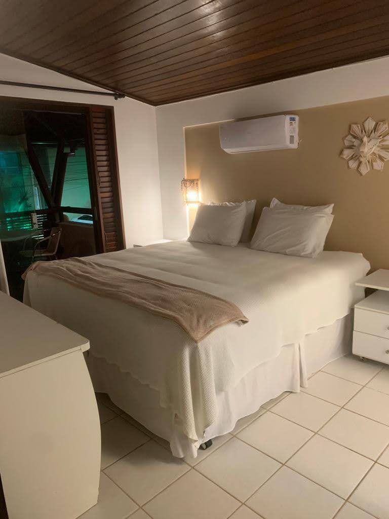 Suíte com roupa de cama clara e luminária de parede